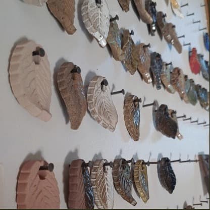 Peças cerâmicas em formato de folhas penduradas na parede do ateliê